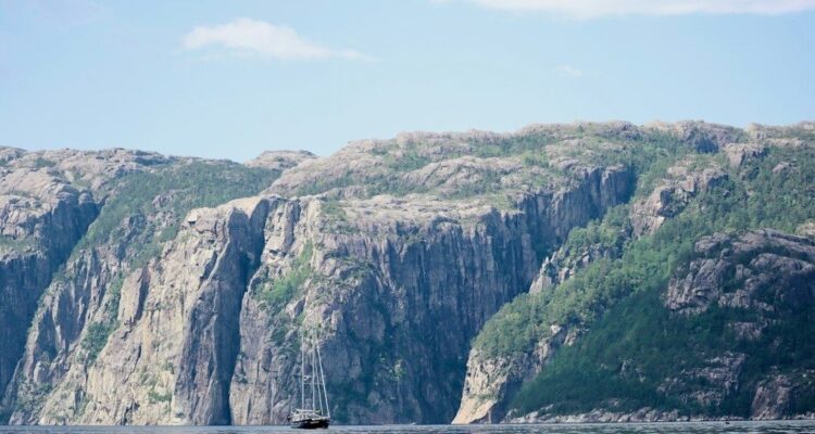 Segelbåt på lugnt vatten framför branta, klippiga kustberg